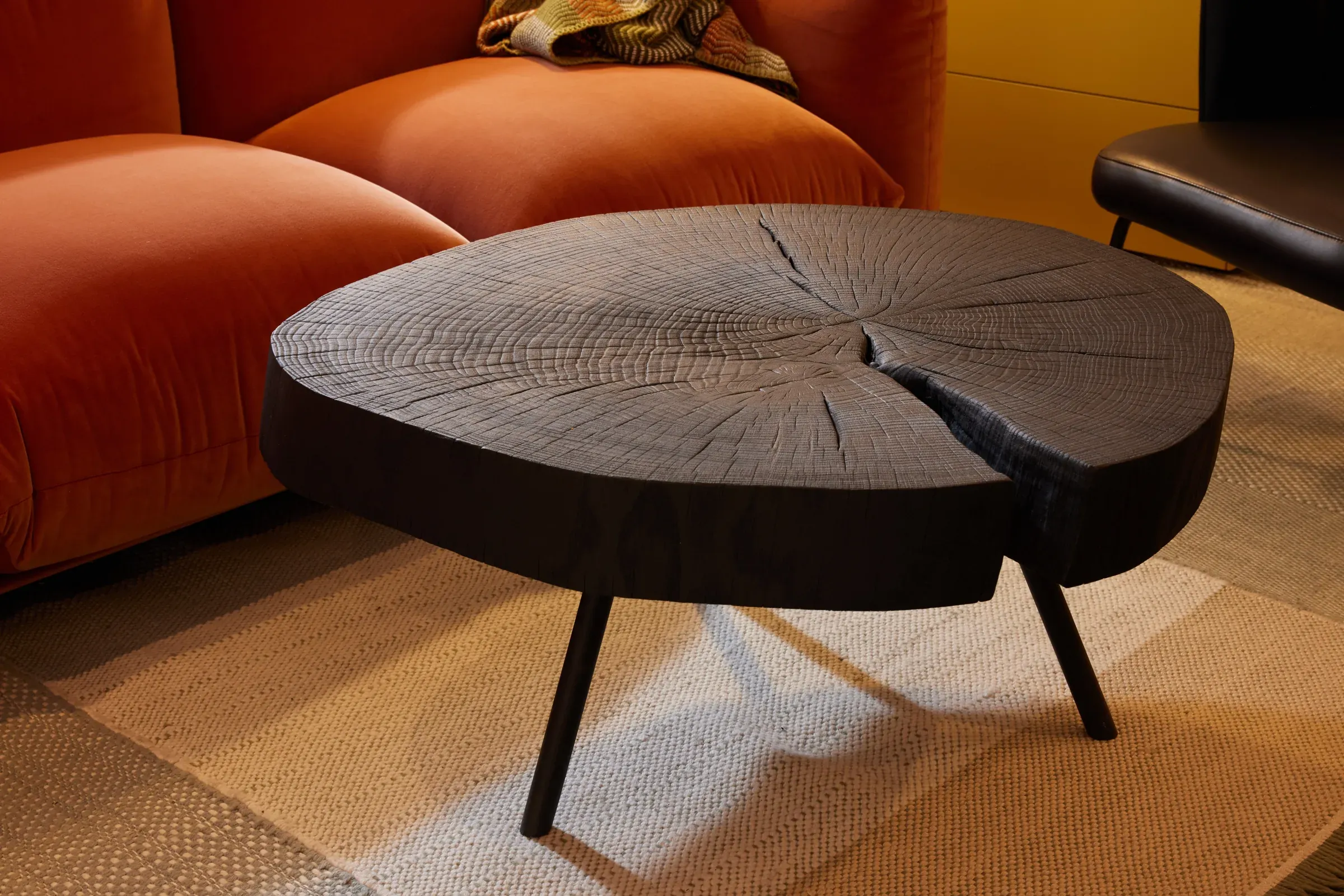 Couchtisch aus einer schwarzen Baumscheibe vor einem Sofa